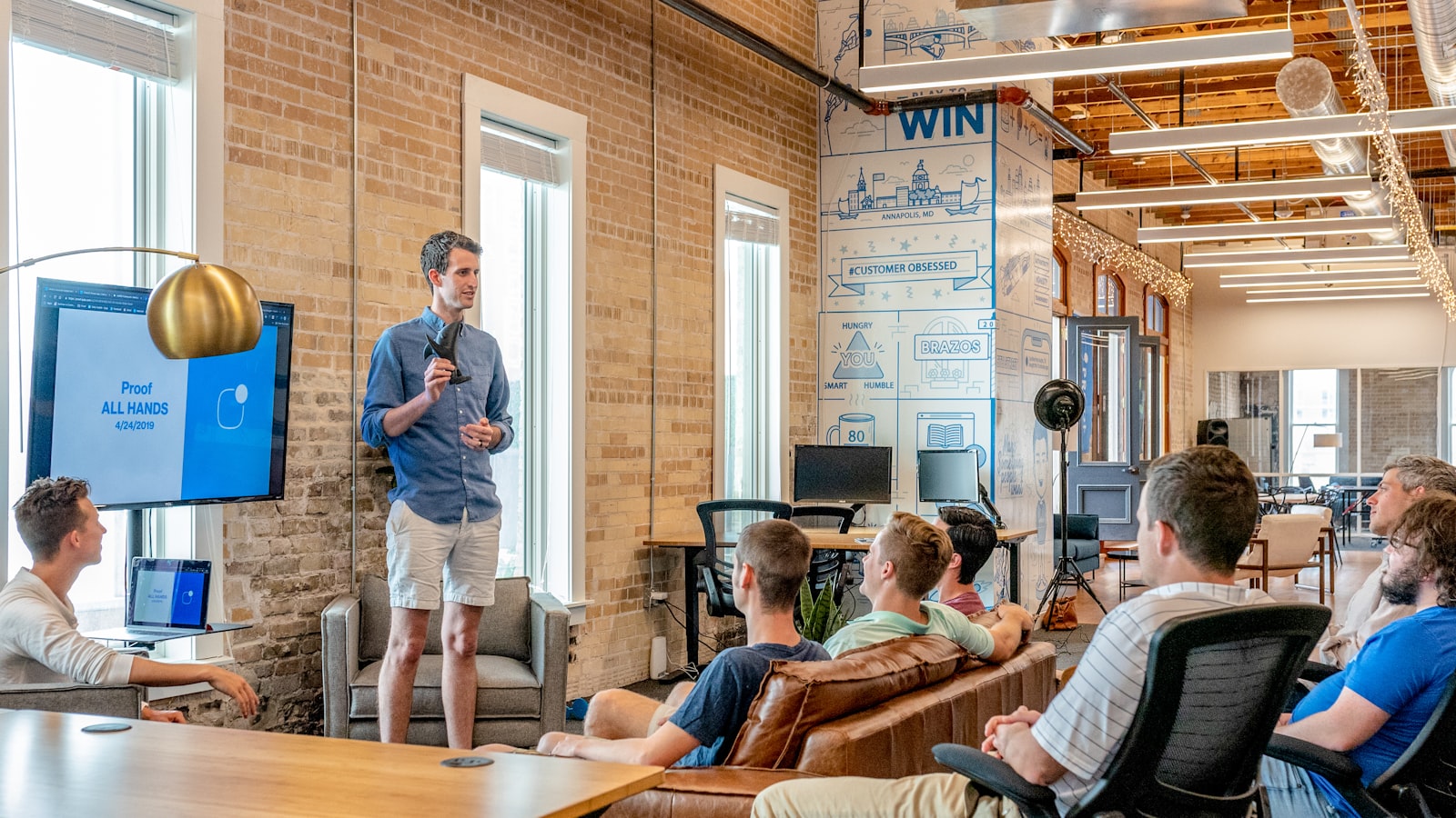 A modern open-plan office with team members in a presentation around a leather couch