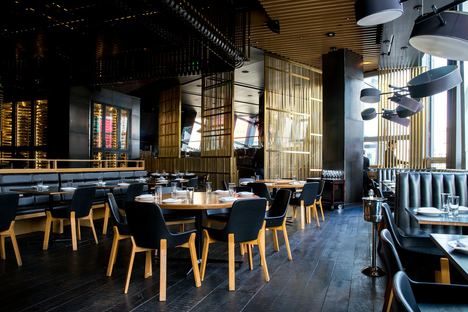 Interior of a restaurant dining room with set tables, warm lighting, and an open kitchen in the background